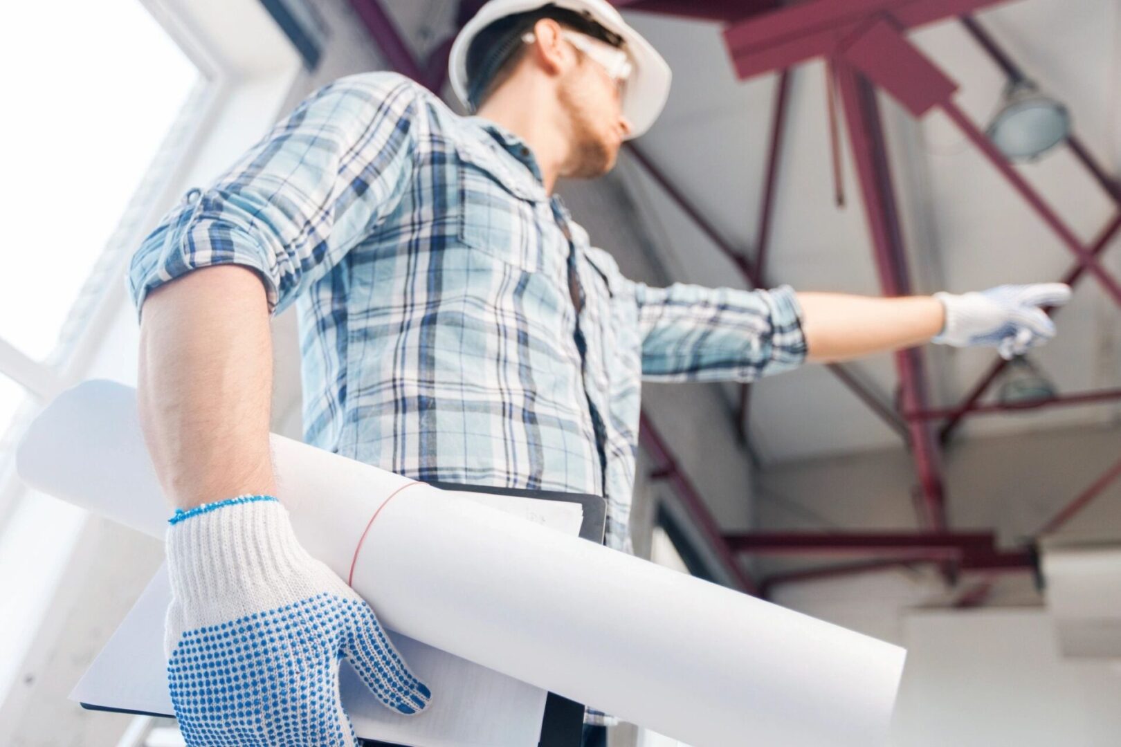 A man in plaid shirt and hard hat holding papers.